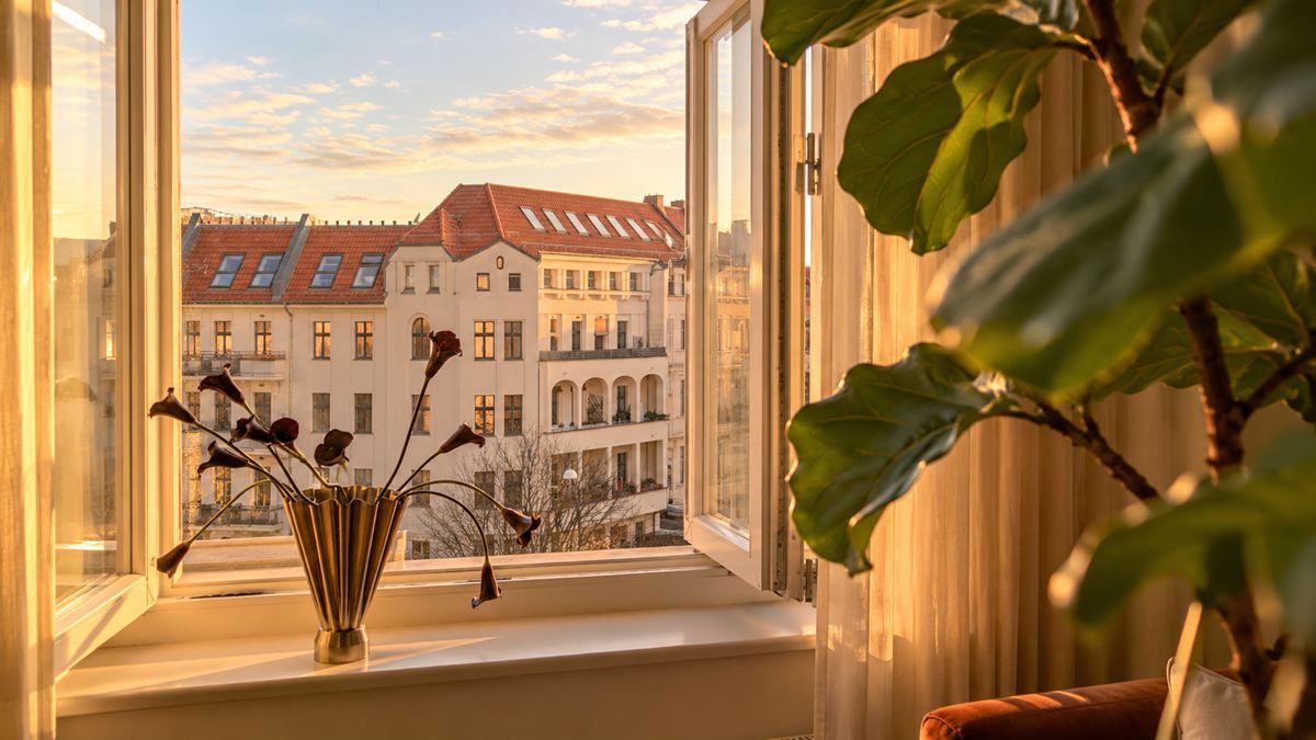 An open window at the practice with a golden vase on the sill; outside, a Berlin period building in the evening light.