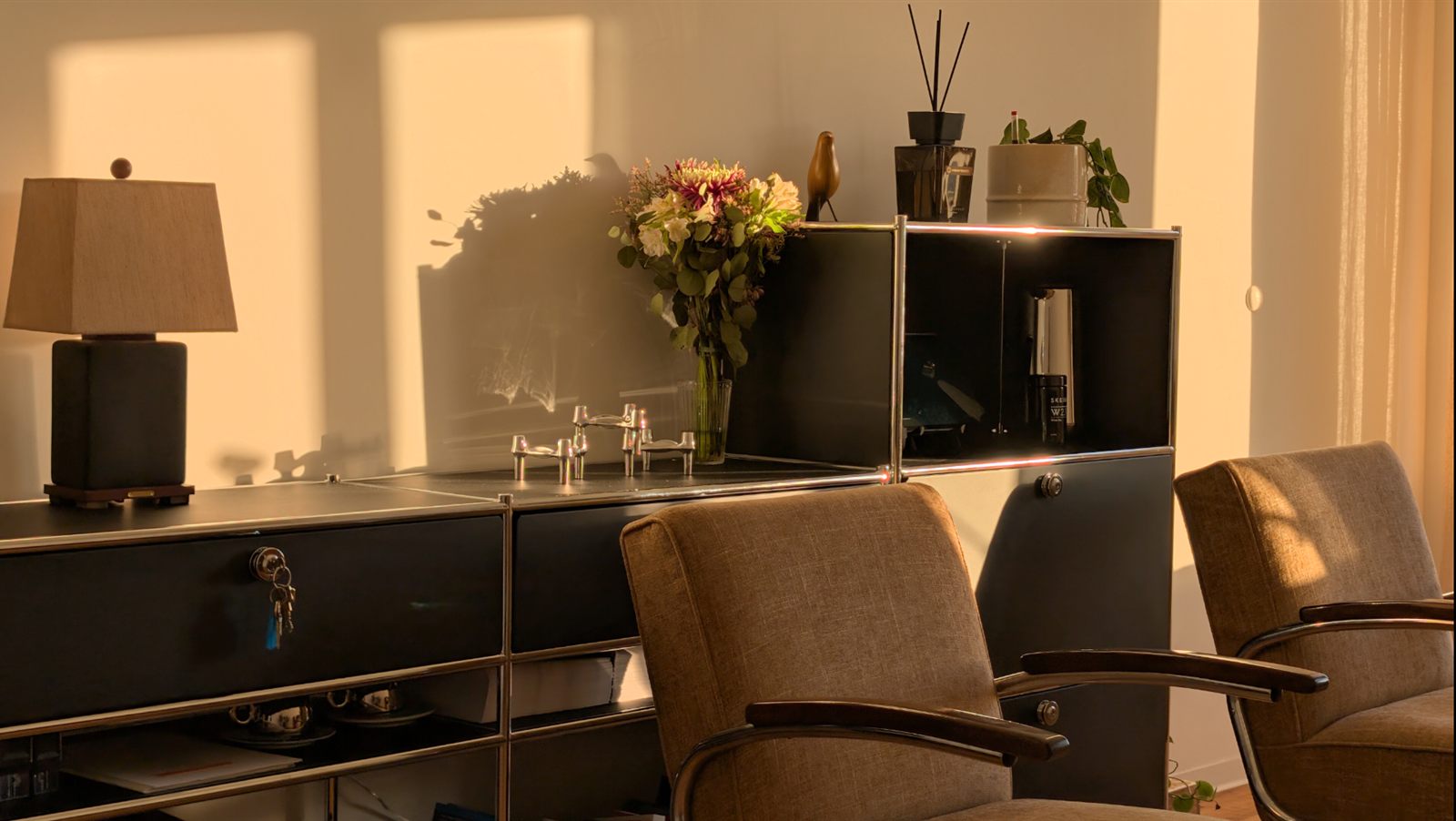 The consulting room in warm evening light: a sideboard with a lamp and flowers, two armchairs in front